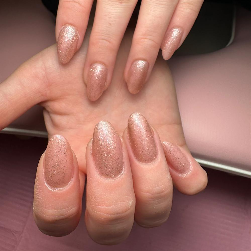 Met acrylgel verlengde amandelvormige nagels in rosé gouden glitter